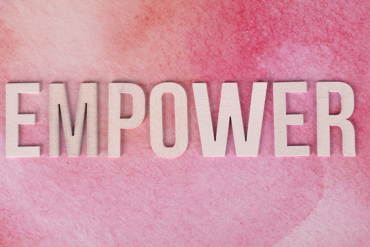 Wooden letters spelling EMPOWER on a pink watercolor background.